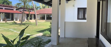 Un patio cubierto con suelo de piedra, un banco de madera y vistas a un edificio con tejado rojo.