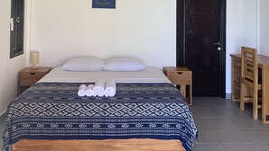 Un dormitorio con una cama, dos mesitas de noche, un escritorio y una puerta.