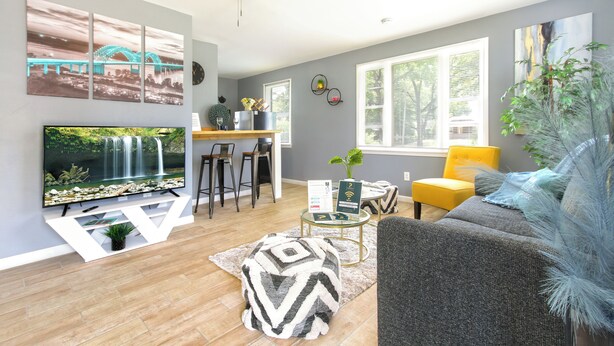A modern living room with a flat-screen TV, a ceiling fan, a dining area with bar stools, and a large window providing natural light. - Serenity Haven with ShellCrestCorp Apt 106 (Memphis)