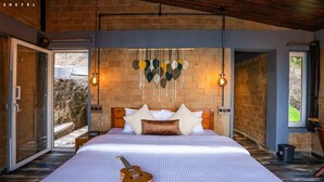 A spacious bedroom with a large bed, a guitar, and a view of the outdoors through a glass door. - Zostel Plus Poombarai (Kodaikanal) (Kodaikanal)