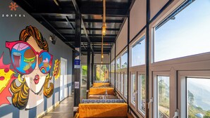 A corridor with benches, a mural, and large windows offering a view of the landscape. - Zostel Plus Poombarai (Kodaikanal) (Kodaikanal)