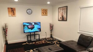A living room with a large flat-screen TV, a clock, and two vases with flowers. - Room in House - Majestic Private Room (Alexandria)