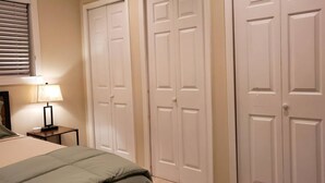 A bedroom with a bed, a nightstand, a lamp, and three white doors. - Room in House - Majestic Private Room (Alexandria)