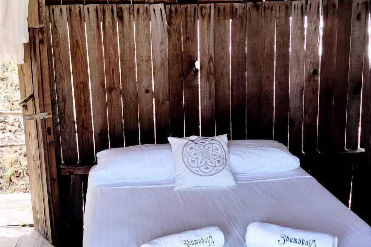 A wooden bed with white linens and two towels with 'Shambhala' printed on them.