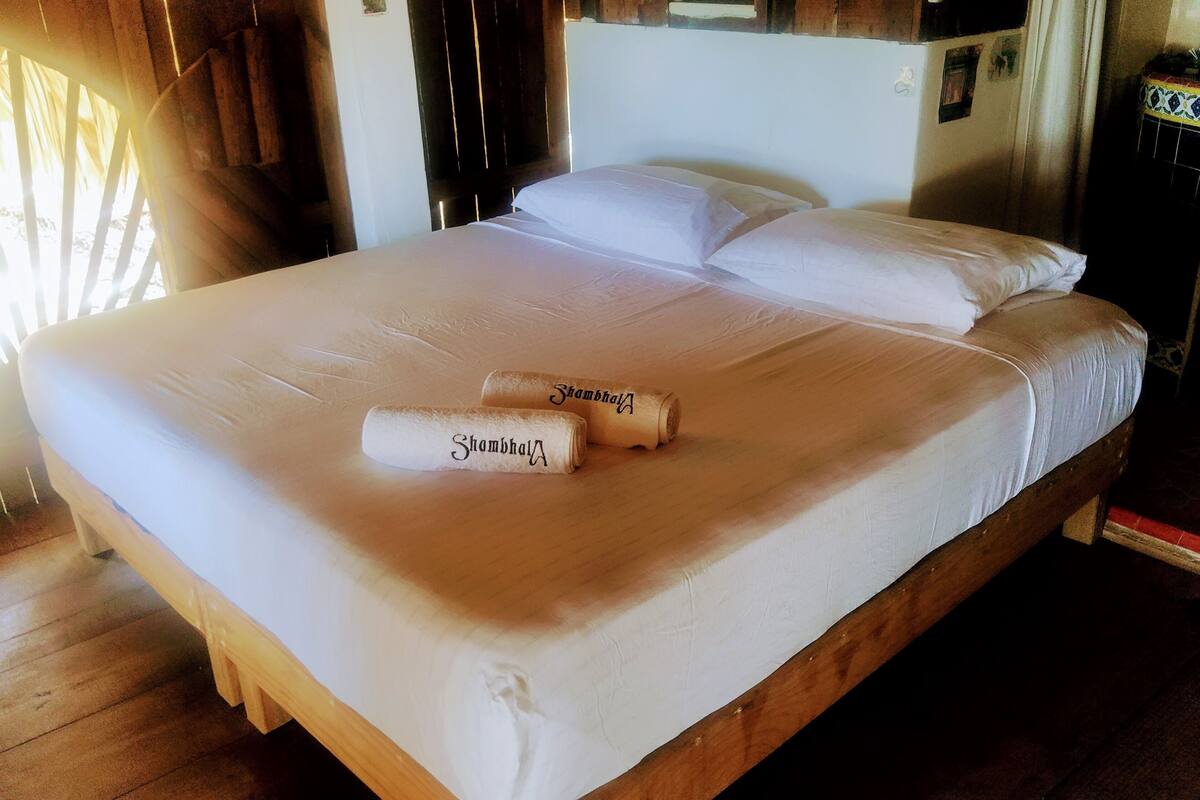 A neatly made bed with two rolled towels labeled "Shambhala" and a wooden headboard.