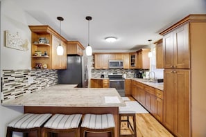 A modern kitchen with wooden cabinets, a marble countertop, and pendant lighting.