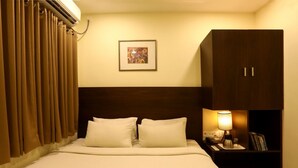 A hotel room with a bed, a nightstand with a lamp, a framed picture on the wall, and a wardrobe. - Blu Ivy Serene Serviced Apartments (Chennai)