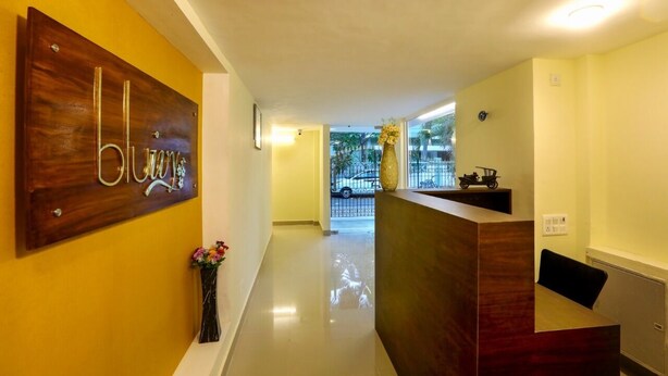 A reception area with a wooden reception desk, a vase with flowers, and a sign with the word "blonde" on the wall. - Blu Ivy Serene Serviced Apartments (Chennai)