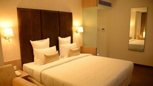 A hotel room with a large bed, two bedside tables, a chair, and a mirror. - Blu Ivy Serene Serviced Apartments (Chennai)