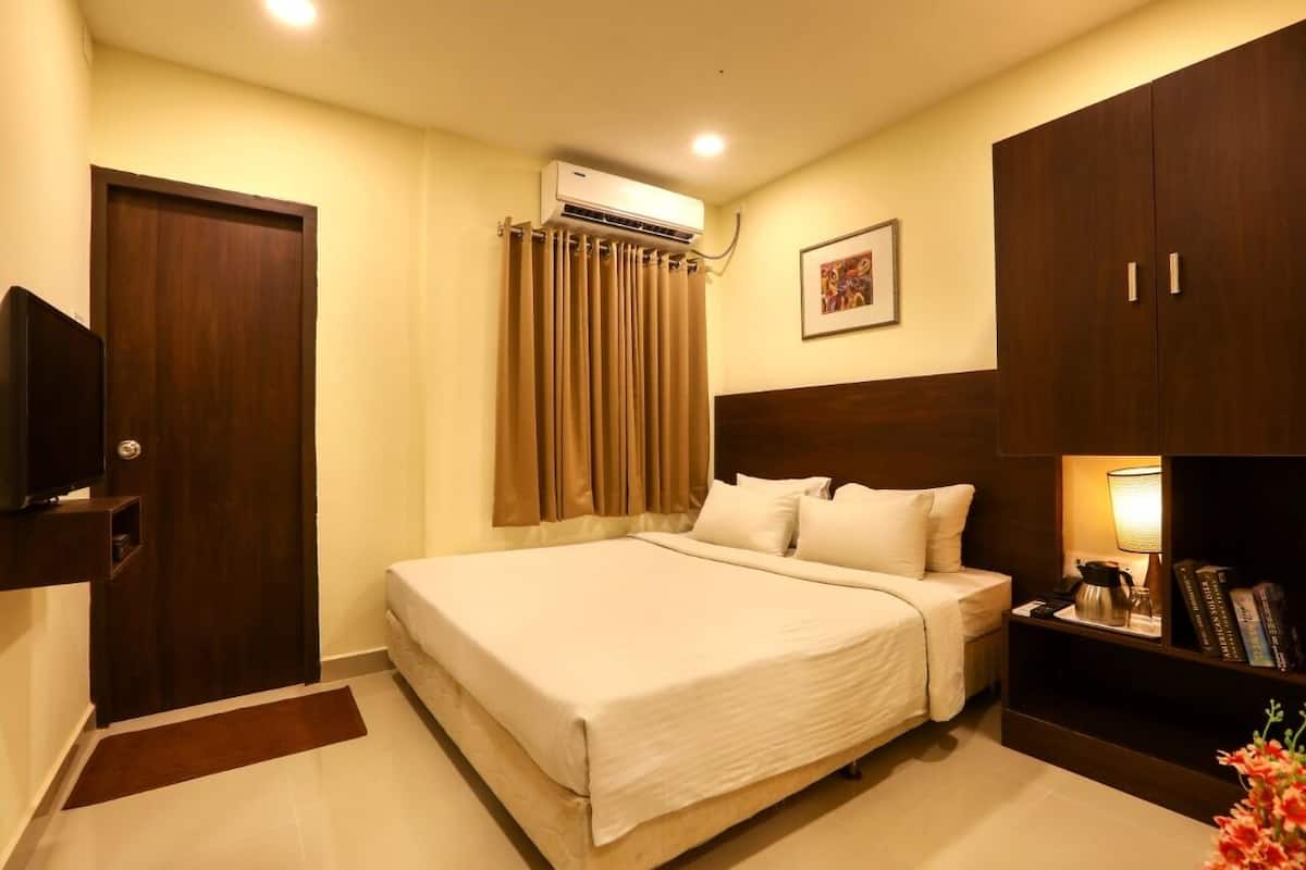 Une chambre d’hôtel comprenant un lit, une armoire, une télévision, un appareil de climatisation et une table de chevet avec une lampe et des livres.