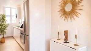 A modern kitchen with a stainless steel refrigerator, a white cabinet, and a decorative sunburst mirror on the wall. - Modern flat near Bercy (Paris)