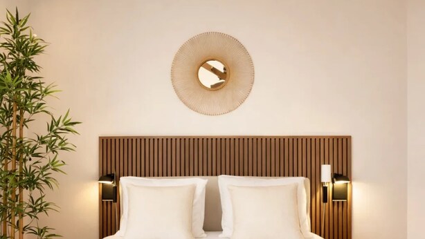 A hotel room with a bed, two pillows, a round mirror, wall-mounted lights, a bamboo plant, and two towels. - Modern flat near Bercy (Paris)