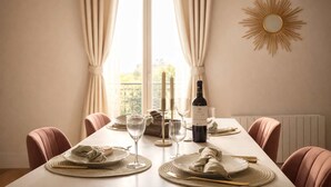 A dining table set with plates, glasses, and a bottle, flanked by chairs, with a window and curtains in the background. - Modern flat near Bercy (Paris)
