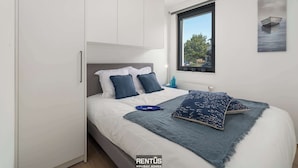 Quarto moderno com cama, guarda-roupa branco e janela com vista para árvores.