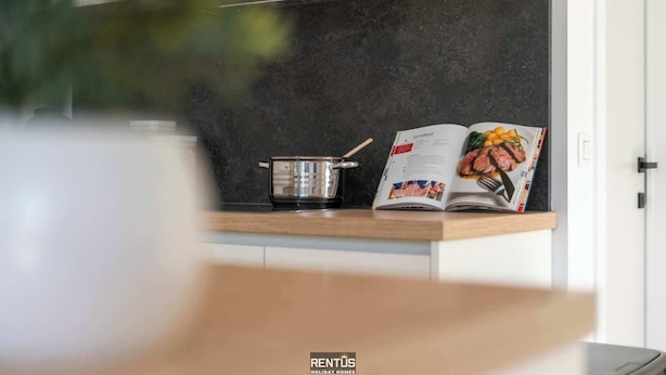 Cozinha moderna com revestimento escuro, uma panela sobre o balcão e uma revista aberta em uma página de receita.