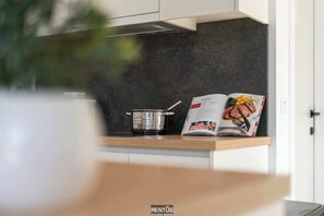 A modern kitchen with a dark backsplash, a pot on the counter, and a magazine open to a recipe page.