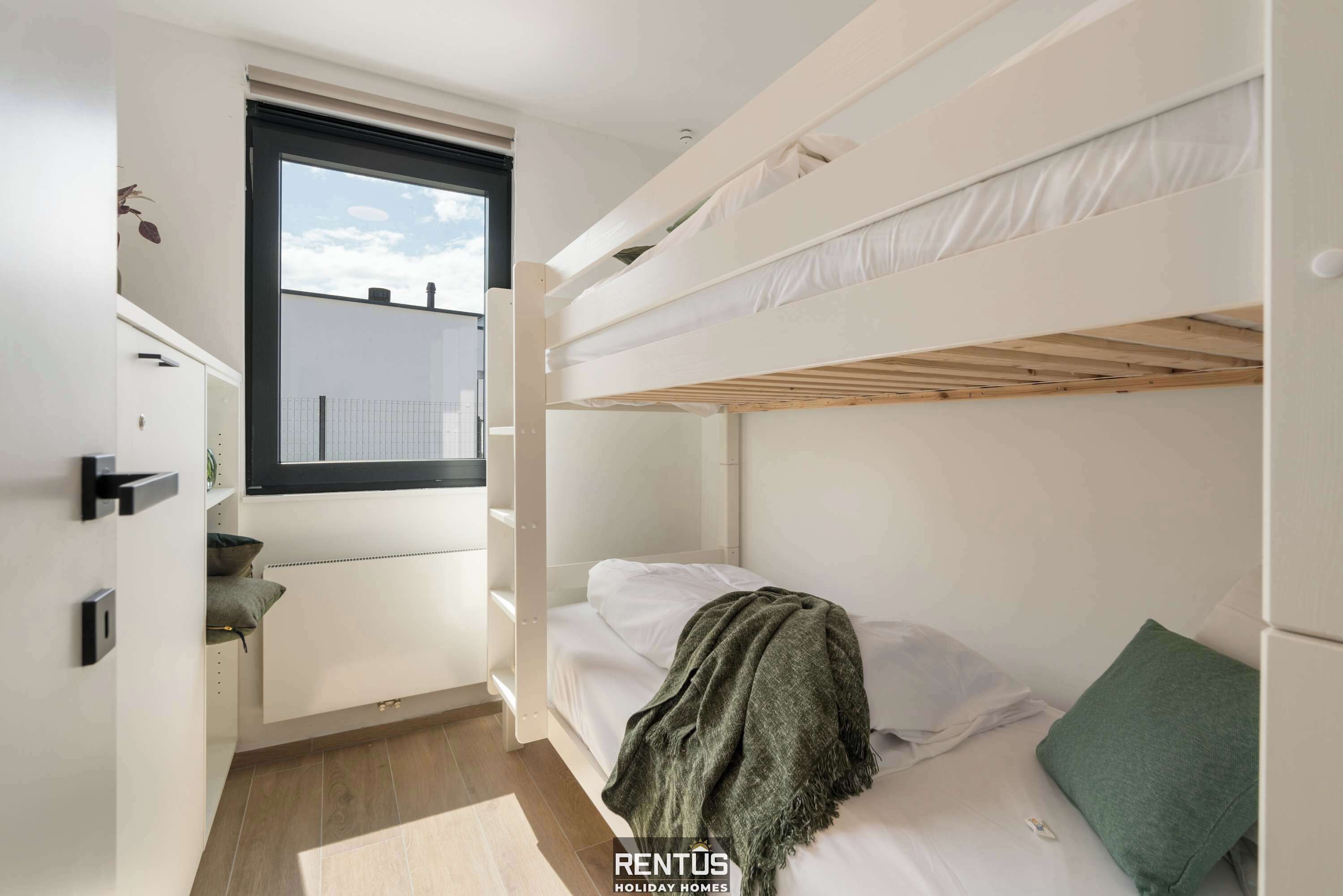 Un dormitorio pequeño con literas, una ventana y almacenamiento integrado.