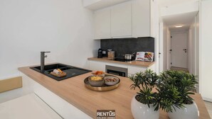 Uma cozinha moderna com pia preta, bancada de madeira e armários brancos. Há duas plantas em vasos sobre a bancada.