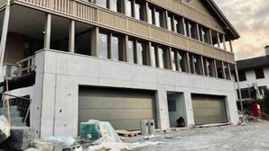 A two-story building with a balcony, large garage doors, and construction materials on the ground. - Chez Marie Lake I Mountains I Fantastic view I Lucerne  (Beckenried)