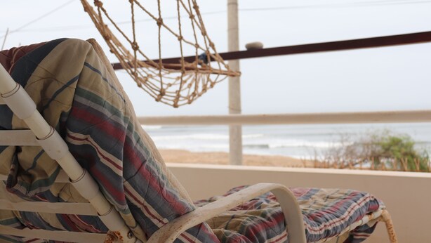 Une chaise de plage avec un coussin rayé, un hamac en corde et une vue sur l’océan.