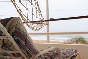 A beachside chair with a striped cushion, a rope hammock, and a view of the ocean.