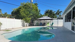 A backyard with a swimming pool, patio furniture, and a covered seating area.