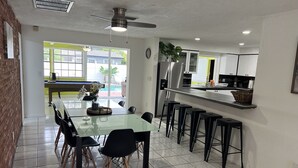 A modern kitchen with a central island, bar stools, and a dining area with a glass table and chairs.