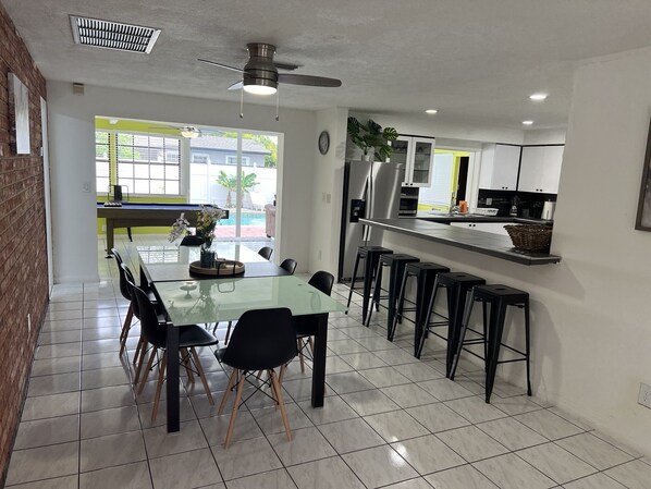 A modern kitchen with a central island, bar stools, and a dining area with a glass table and chairs.
