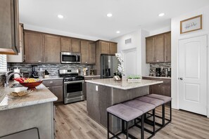 A modern kitchen with wooden cabinets, stainless steel appliances, a marble countertop, and a central island with seating. - Luxury Desert Hot Springs 4BR/3BA Vacation Home /Private Pool & Mountain Views (Desert Hot Springs)
