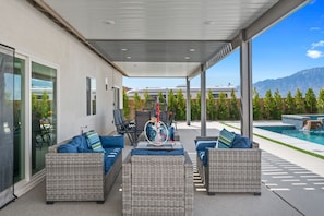 A covered outdoor seating area with wicker furniture and a pool in the background. - Luxury Desert Hot Springs 4BR/3BA Vacation Home /Private Pool & Mountain Views (Desert Hot Springs)