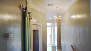 A hallway with a door leading to a kitchen, a chandelier, and a view into another room. - Garden District | Steps to St. Charles Streetcar (New Orleans)
