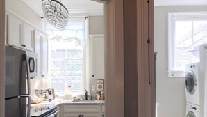 A compact kitchen with white cabinets, a refrigerator, a sink, and a washing machine. - Garden District | Steps to St. Charles Streetcar (New Orleans)