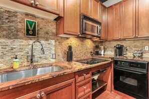 A kitchen with wooden cabinets, a brick backsplash, stainless steel sink, and modern appliances including a microwave and dishwasher.