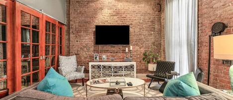 Un salon chaleureux avec un mur en briques, un téléviseur à écran plat, une table basse ronde et des sièges confortables.