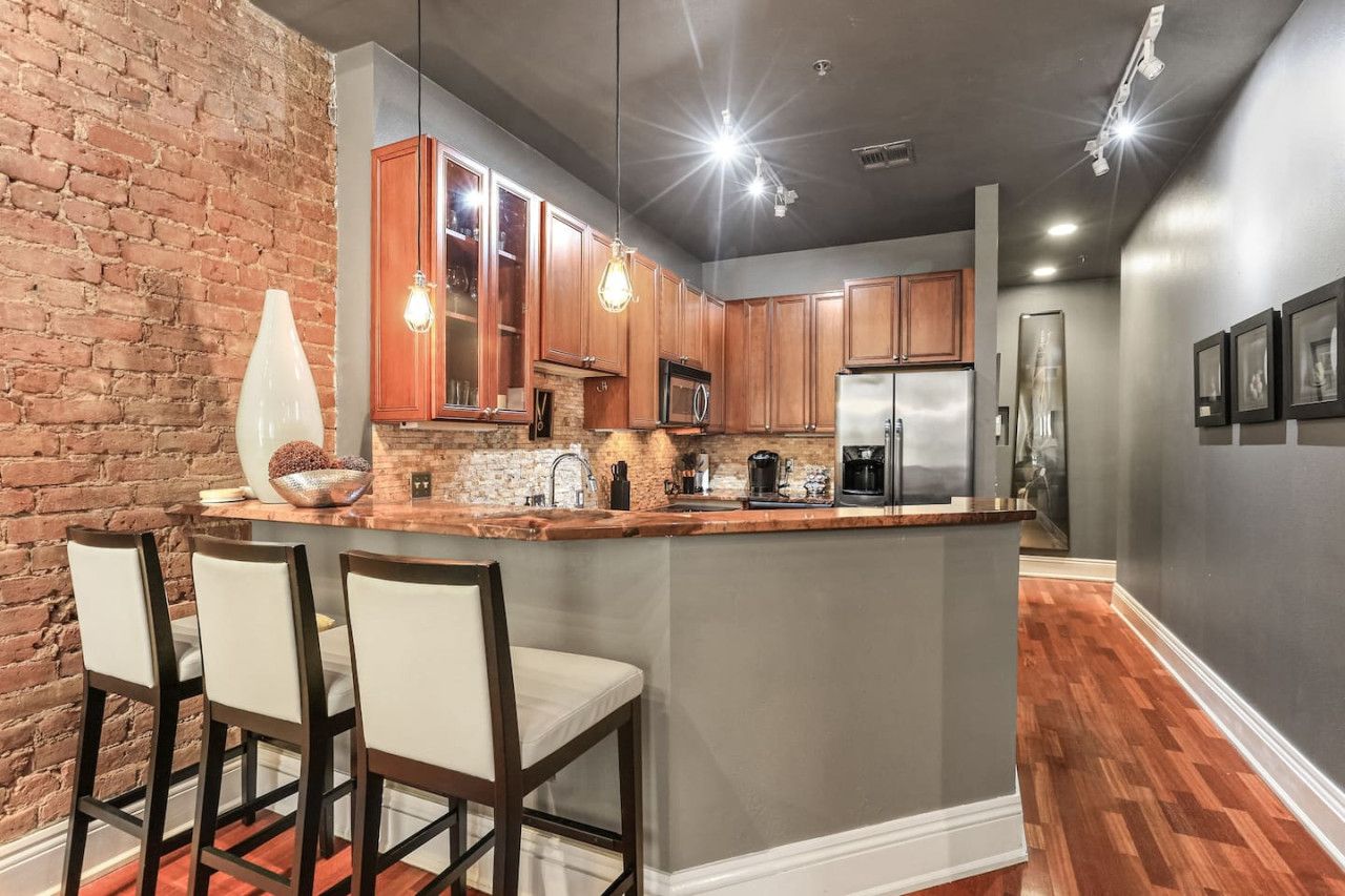 A modern kitchen with a central island, wooden cabinets, and a brick accent wall.