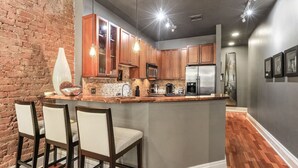 Een moderne keuken met een centraal eiland, houten kasten en een accentmuur van baksteen.