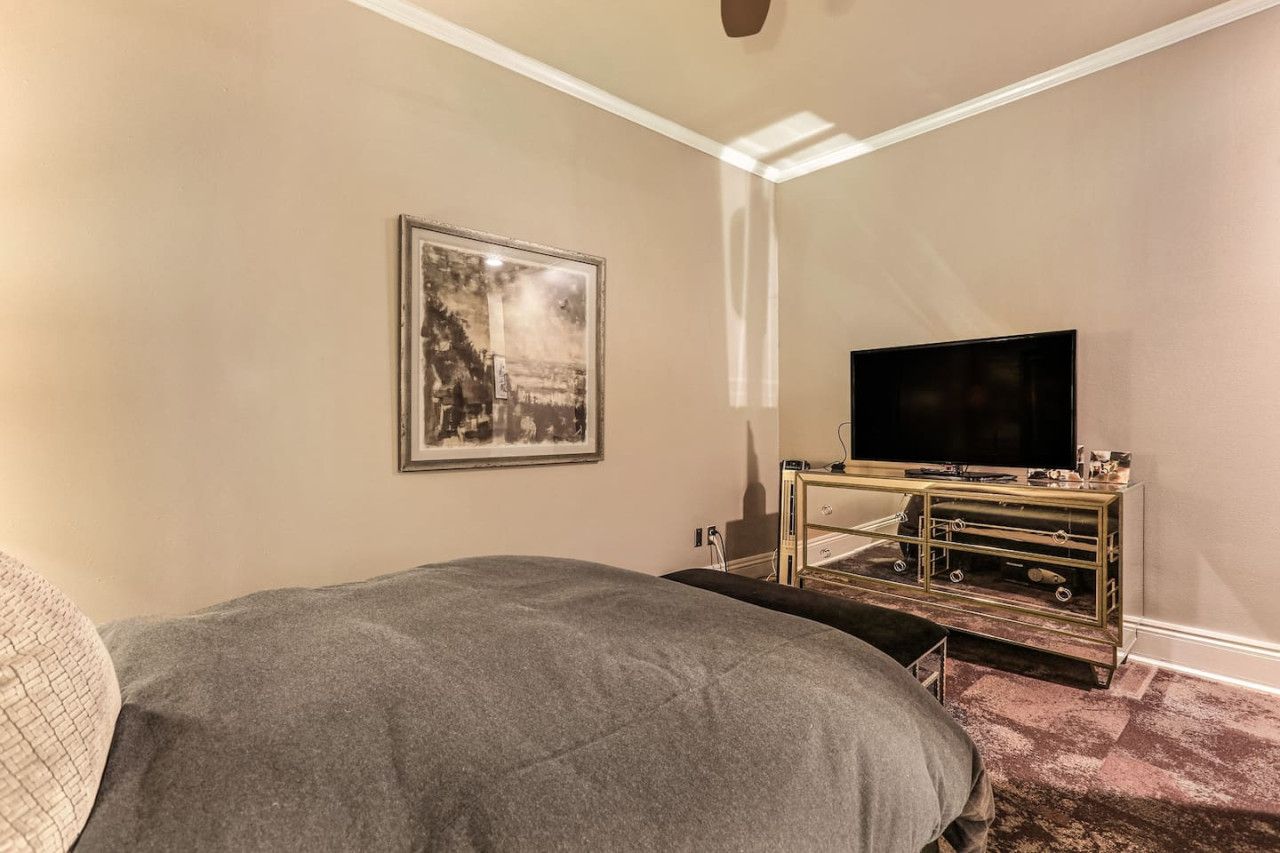 Un dormitorio con una cama, un televisor sobre un mueble bajo y un cuadro en la pared.