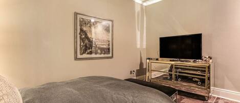 Un dormitorio con una cama, un televisor sobre un mueble bajo y un cuadro en la pared.
