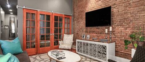 A living room with a brick wall, a flat-screen TV, a sofa, a coffee table, and a cabinet.
