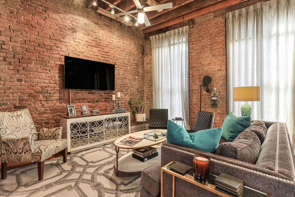 A living room with a brick wall, a flat-screen TV, a sofa, a chair, a coffee table, and a sideboard.