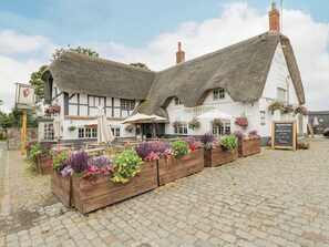A traditional thatched-roof building with outdoor seating and flower planters.