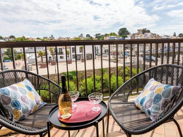 A balcony with two wicker chairs, a small round table, a bottle of wine, and two wine glasses.
