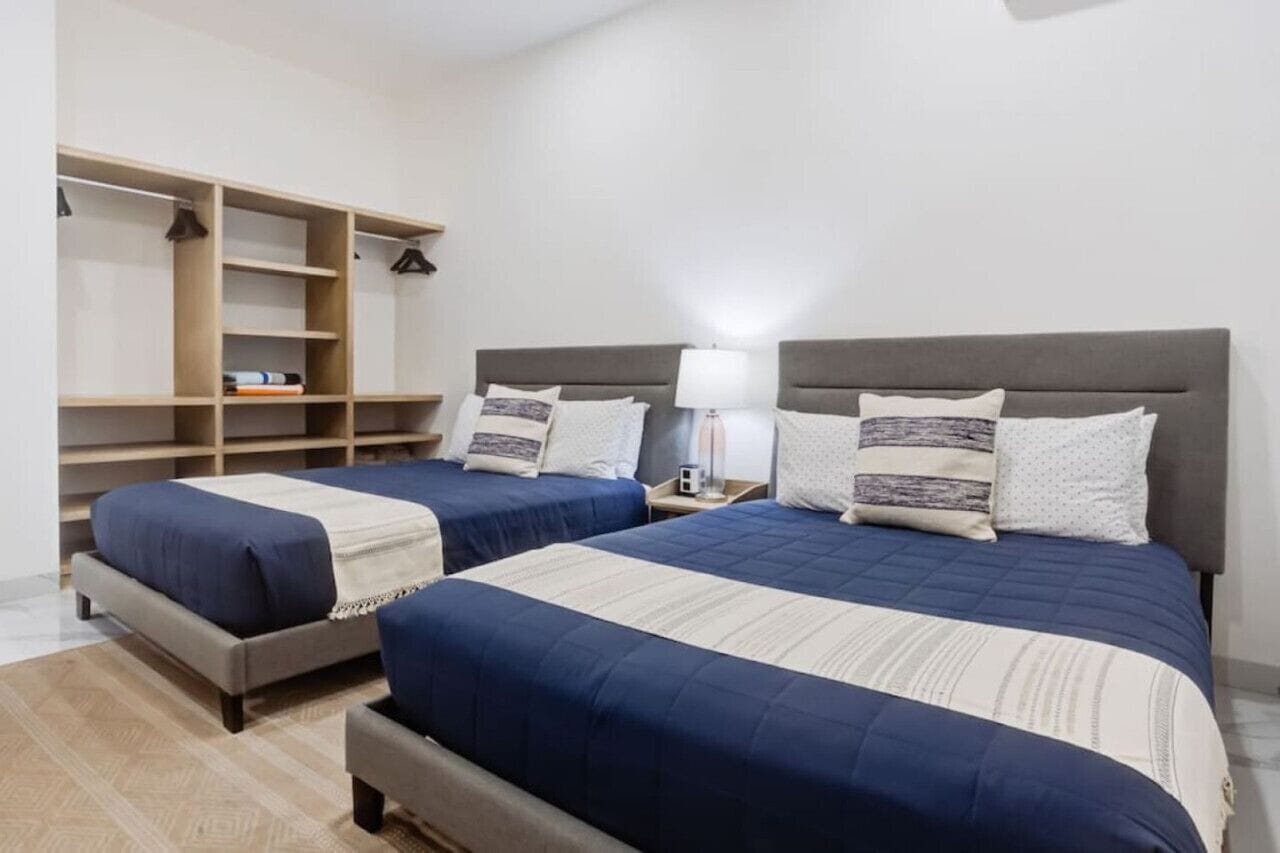 A hotel room with two beds, a wardrobe, and a bedside table with a lamp.