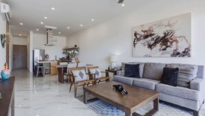 A modern living room with a grey sofa, a wooden coffee table, and a dining area with wooden chairs and a table. - Elite Ocean View Retreat+ Roof Pool (Cabo San Lucas)