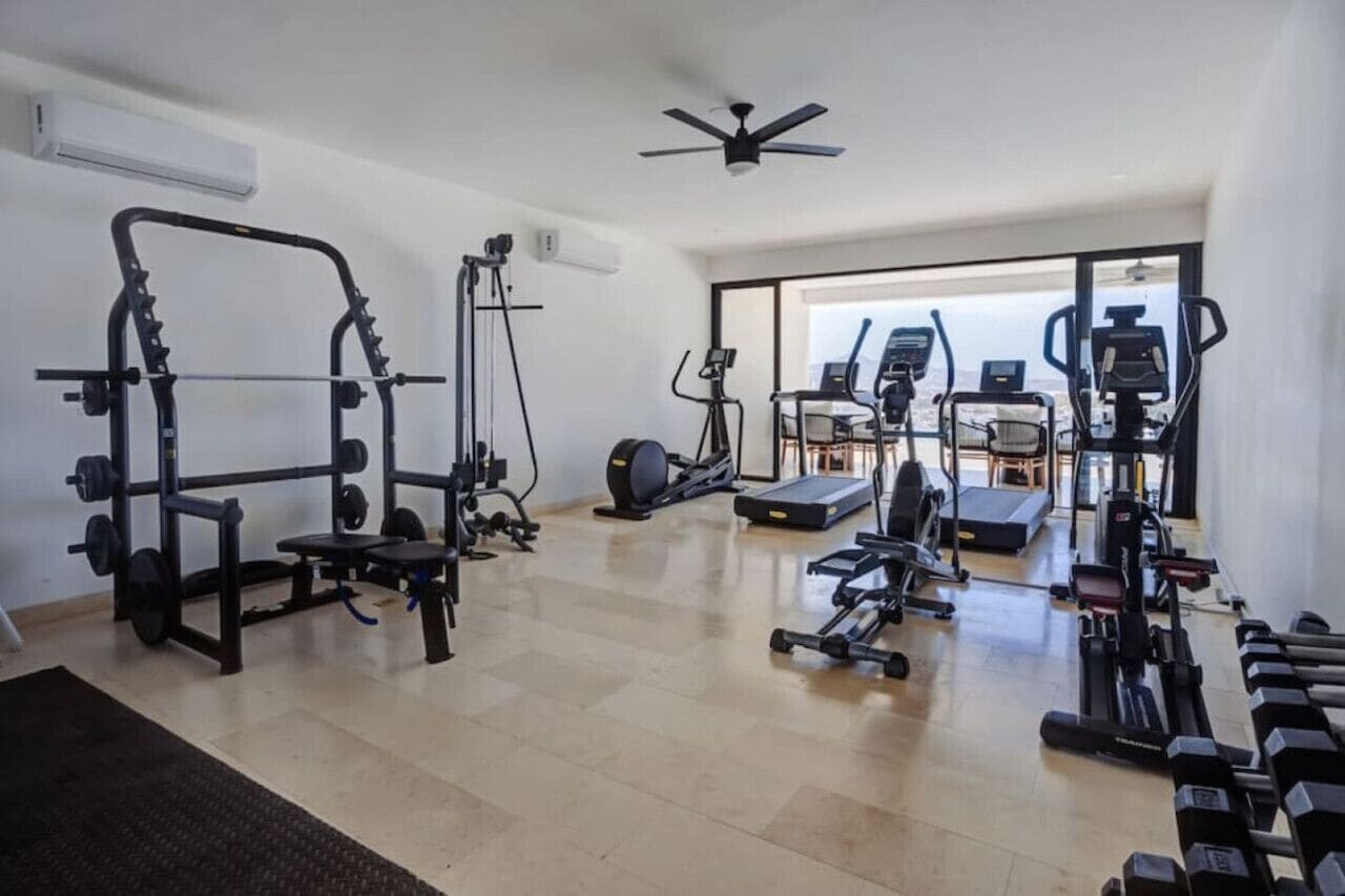 Une salle de sport équipée de divers appareils, notamment un support à squats, un tapis de course et des poids.