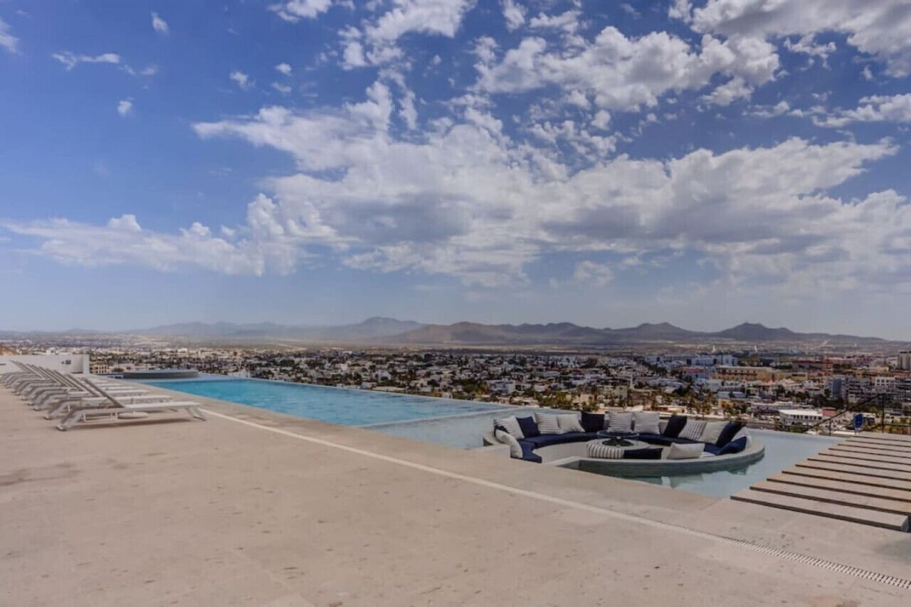 A rooftop pool with lounge chairs and a view of a cityscape and mountains in the distance.