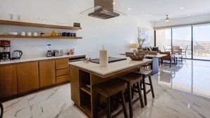 A modern kitchen with wooden cabinets, a central island with stools, and a large window offering a city view. - Elite Ocean View Retreat+ Roof Pool (Cabo San Lucas)