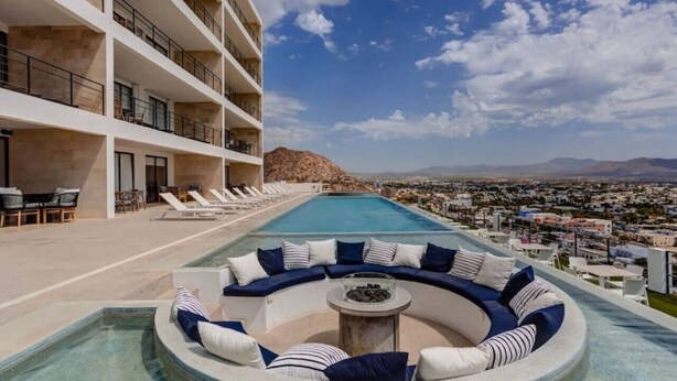 A rooftop infinity pool with a curved seating area and a view of a cityscape and mountains. - Elite Ocean View Retreat+ Roof Pool (Cabo San Lucas)