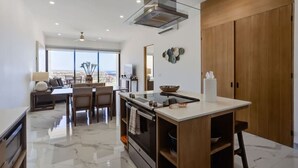 A modern kitchen with a central island, a dining area with a view, and a large wooden wardrobe. - Elite Ocean View Retreat+ Roof Pool (Cabo San Lucas)