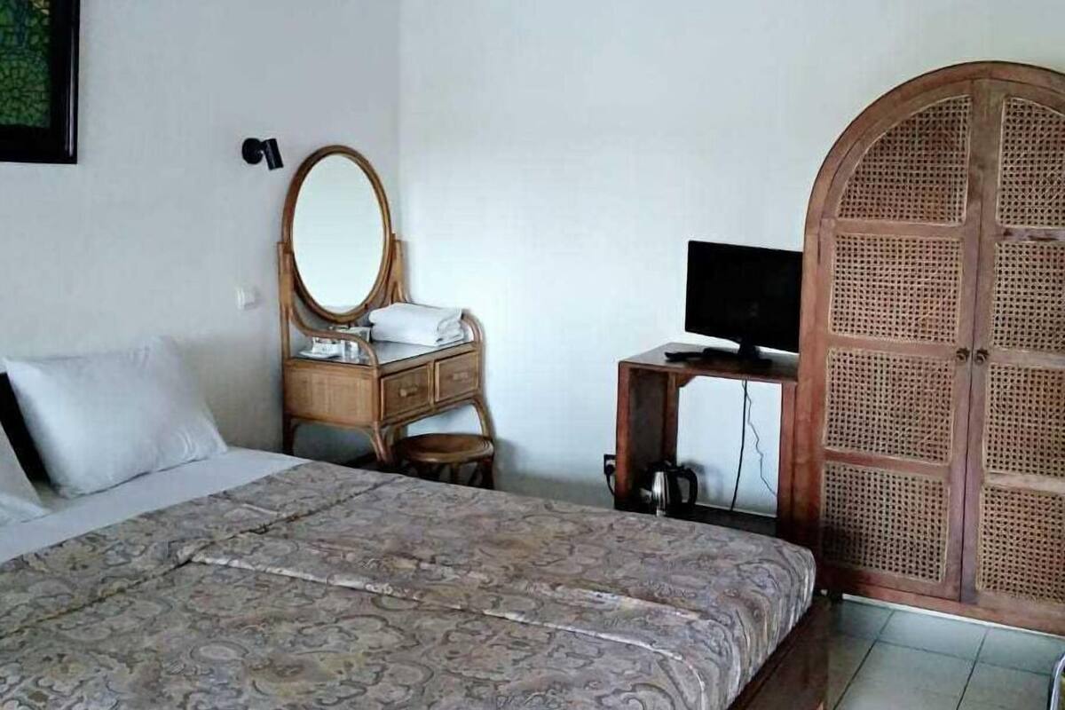 A bedroom with a large bed, a wooden dresser, a round mirror, a television on a small table, and a rattan wardrobe.